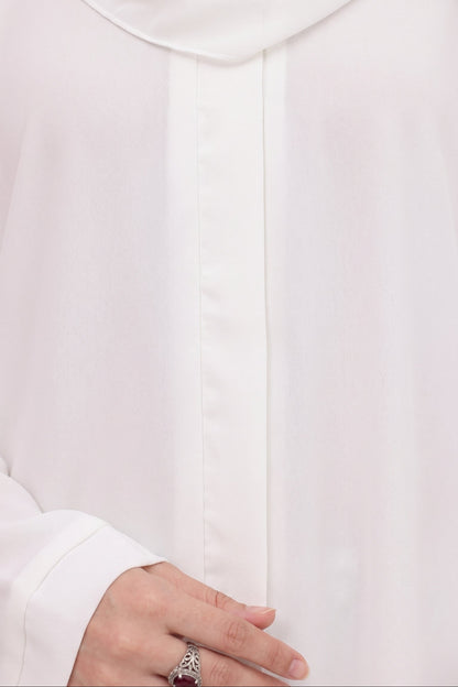 Close-up of a person wearing a white long-sleeve top or abaya with a matching white headscarf, showing the fabric texture and a hand with a ring at the lower left.
