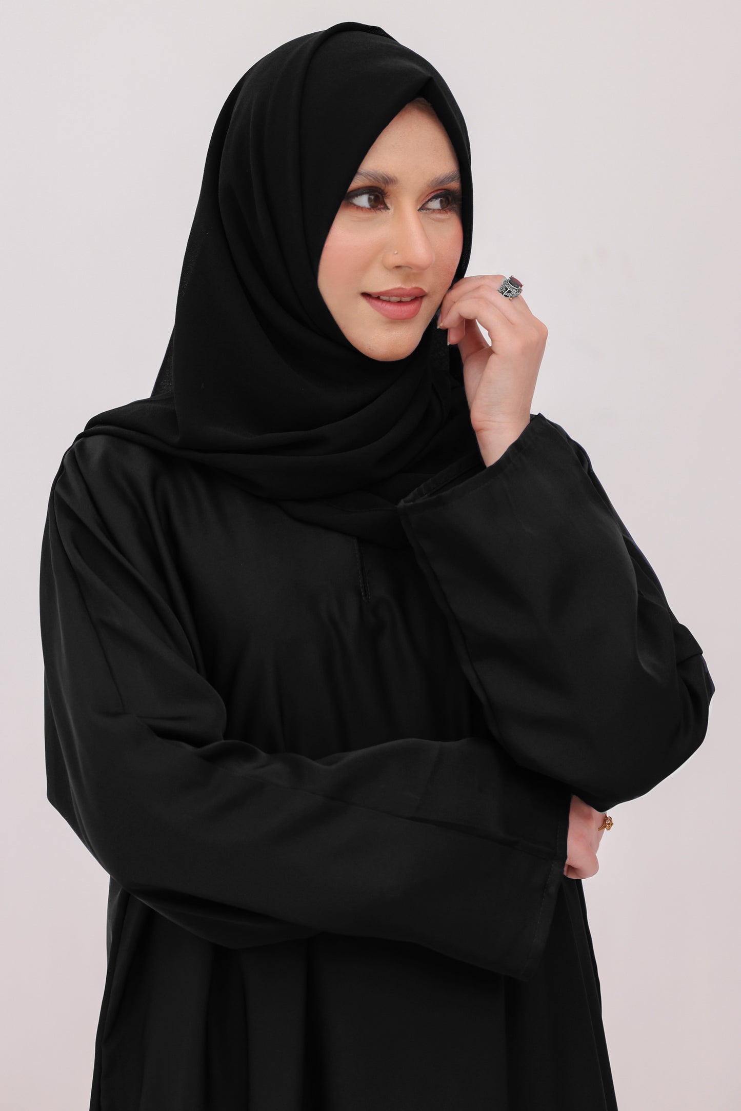 Woman wearing a black hijab and black outfit against a light background