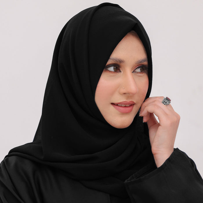 Woman wearing a black hijab and black outfit against a light background
