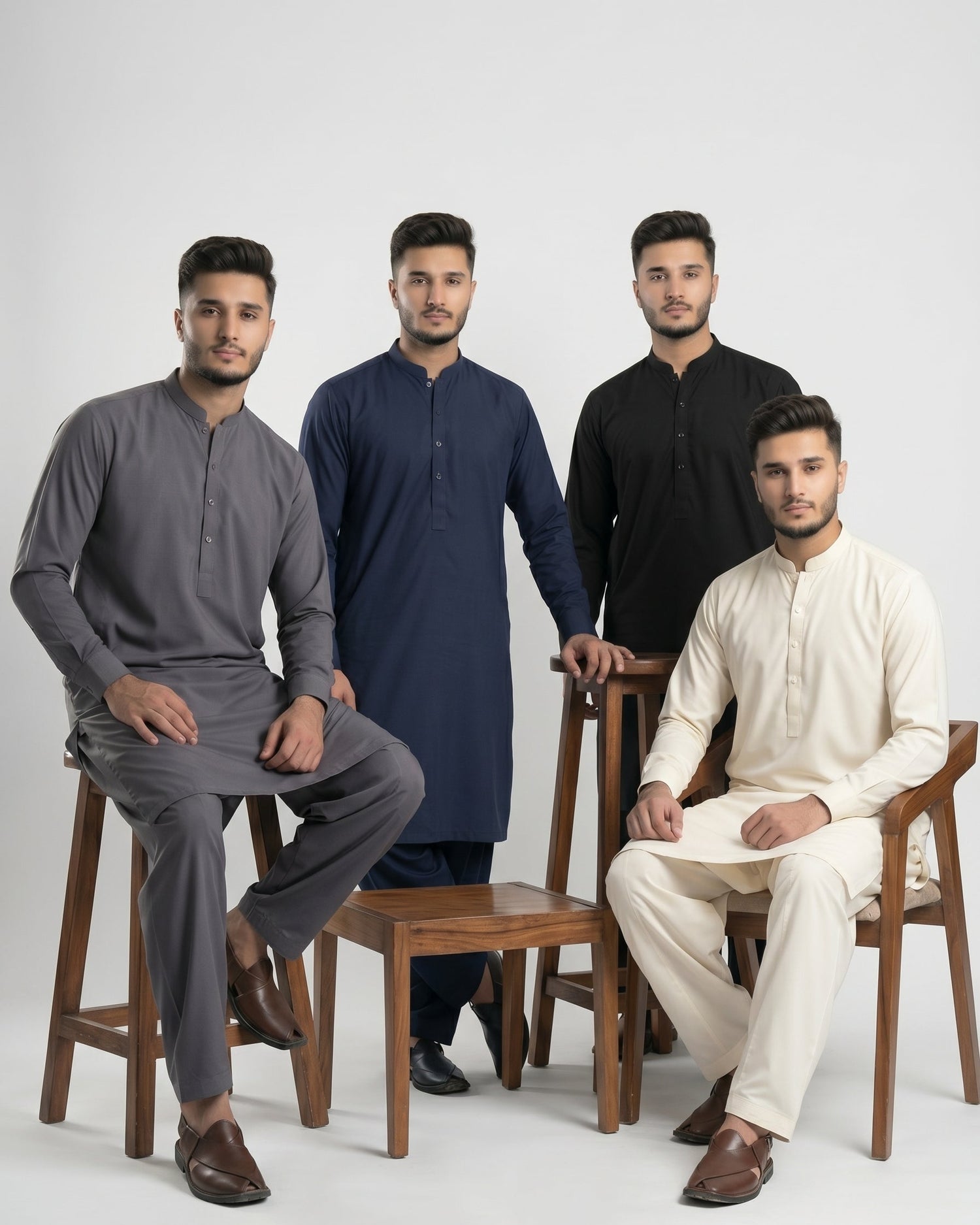 Four men sitting on wooden stools wearing kurta-style outfits against a white background